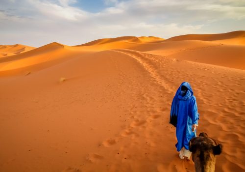 Berber leading a camel into the stunning sand dunes of Sahara desert in Merzouga, Morocco